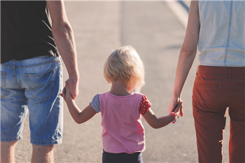 an image of a family, parents on either side holding a child's hands